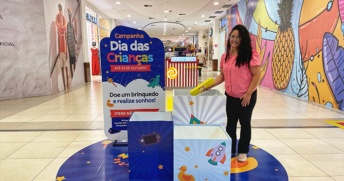 Mulher ao lado do ponto de arrecadação de brinquedos no shopping da ALLOS.